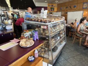 Goldmans Deli interior with a glass display case filled with donuts and pastries and customers seated at tables behind it.